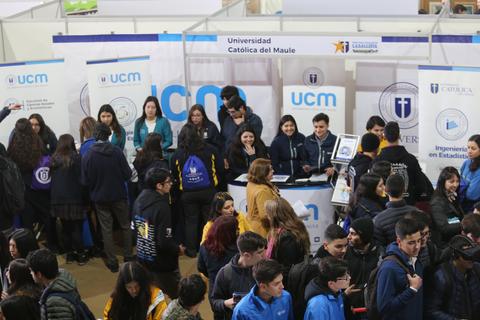 Un grupo de estudiantes se encuentra en un stand de la Universidad Católica del Maule durante una feria educativa.