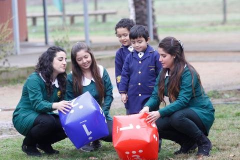 Un grupo de niños y adultos participan juntos en una actividad al aire libre utilizando dados grandes de colores.