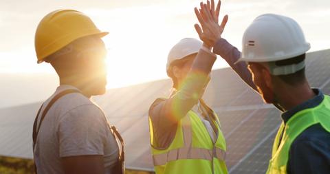 Un grupo de trabajadores celebra su éxito en una planta solar al atardecer.