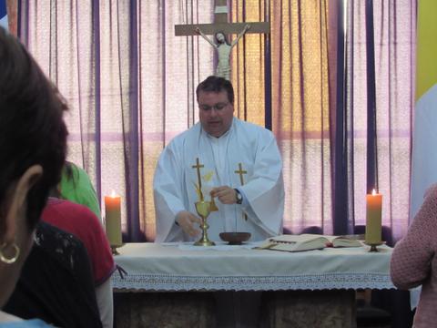Un sacerdote oficiando una misa frente a un altar con velas y un crucifijo de fondo.
