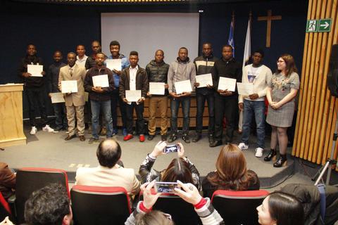 Un grupo de jóvenes sonrientes con certificados se posiciona en un escenario durante un evento de entrega de premios.