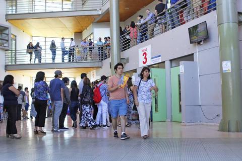 Un grupo de personas se encuentra en un pasillo con múltiples niveles en un edificio, algunos de pie y otros caminando.