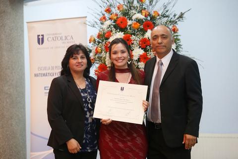 Una celebración de graduación con una estudiante mostrando su diploma junto a sus padres frente a un arreglo floral.