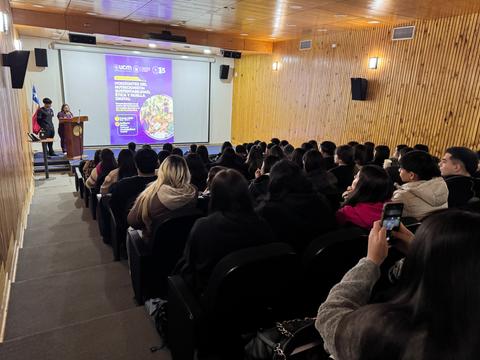 Una charla en un auditorio con un gran número de asistentes atentos a la presentadora.