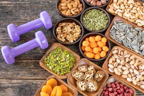 La imagen muestra una variedad de frutos secos y pesas moradas sobre una mesa de madera.