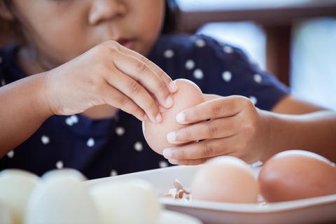 Una niña rompe un huevo en una mesa llena de huevos.