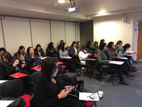 Un grupo de mujeres sentadas en un aula, prestando atención a una presentación.