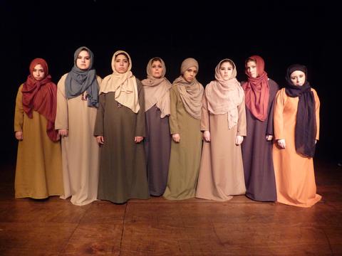 Un grupo de mujeres vestidas con túnicas y pañuelos en la cabeza, posando en un escenario oscuro.