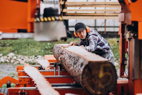 Un hombre trabaja en una sierra de cinta, posando una madera sobre la máquina.