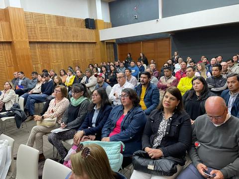 Una multitud de personas sentadas en un auditorio prestando atención a una presentación.