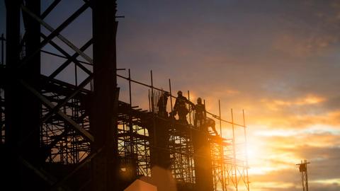 Al atardecer, trabajadores realizan actividades en una construcción con andamios.