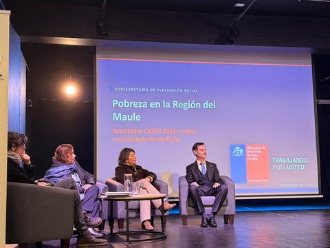 Un panel de discusión sobre pobreza en la Región del Maule, con cuatro personas sentadas en un escenario.