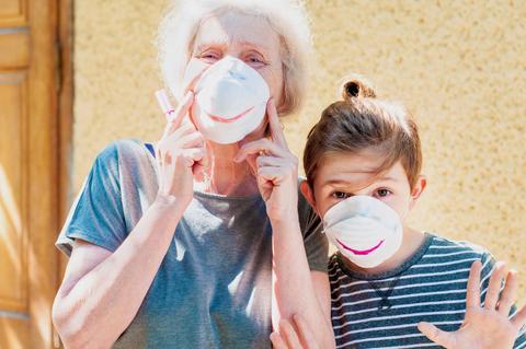 Una mujer mayor y una niña posan con mascarillas que tienen dibujos de sonrisas.