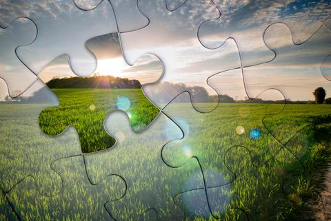 Un paisaje de campos verdes con un sol brillante detrás de un rompecabezas parcialmente armado.