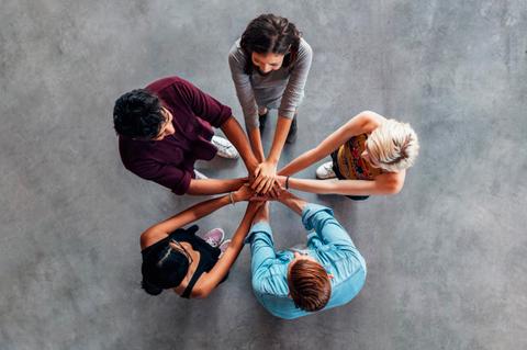 Un grupo de cinco personas uniendo sus manos en el centro, simbolizando unidad y colaboración.