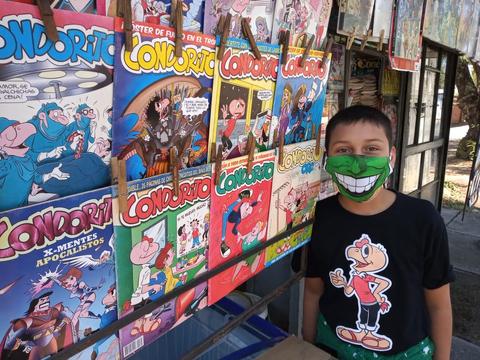 Un niño sonriente junto a un puesto de revista que exhibe varias ediciones de 'Condorito'.