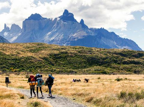 Un grupo de senderistas camina por un sendero rodeado de montañas y pastizales.