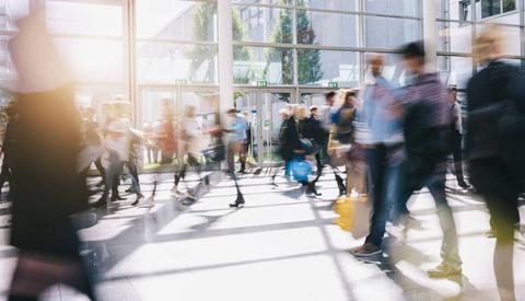 Un gran número de personas camina rápidamente en un espacio abierto y luminoso.