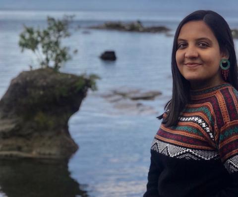 Una mujer sonriente posa junto a un cuerpo de agua con un fondo natural.