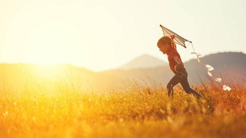 Un niño corre alegremente en un campo al atardecer, volando una cometa.