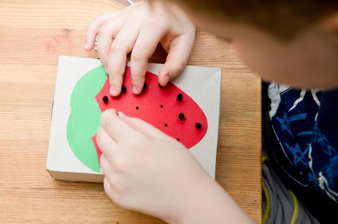 Un niño está jugando con una caja decorada como una fresa.