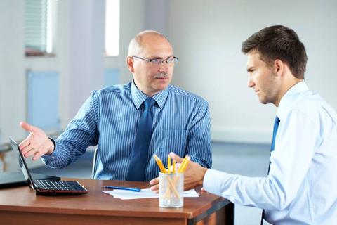 Dos hombres están discutiendo en una oficina mientras trabajan en una computadora portátil.