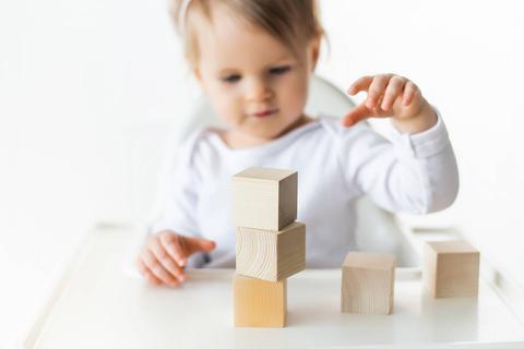 Un niño pequeño está jugando con bloques de madera apilándolos sobre una mesa.