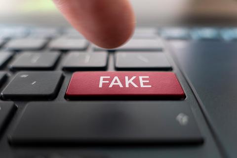 Una mano presiona la tecla roja con la palabra 'FAKE' en un teclado de computadora.