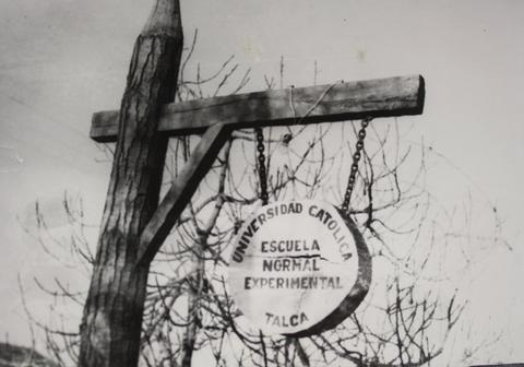 Se observa un letrero de madera que indica la Universidad Católica y la Escuela Normal Experimental en Talca.