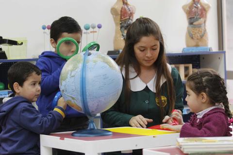 Un grupo de niños juega y aprende con un globo terráqueo junto a una educadora en un aula.
