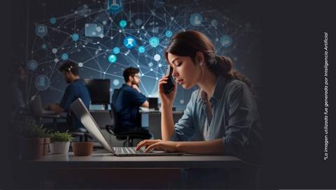 Una mujer trabaja en su computadora portátil mientras habla por teléfono en un entorno de oficina moderna con tecnología conectada.