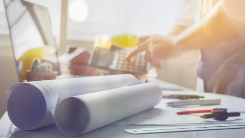 Una persona trabaja en una mesa con planos y herramientas de diseño.