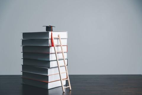 Una pila de libros con un gorro de graduación en la parte superior y una escalera al lado.