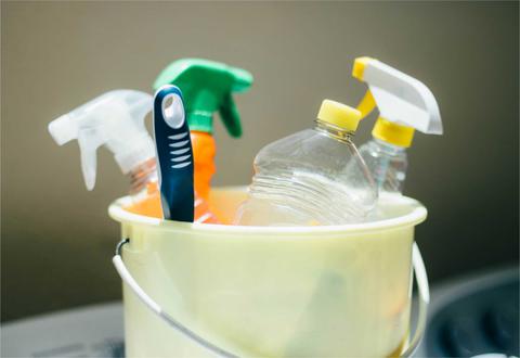 Un cubo amarillo contiene varios productos de limpieza y botellas de plástico.