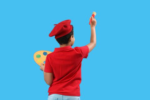 Un niño con un gorro rojo sostiene un pincel y una paleta de colores mientras mira hacia atrás.