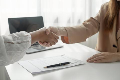 Dos personas estrechan manos en un entorno profesional con documentos sobre la mesa.