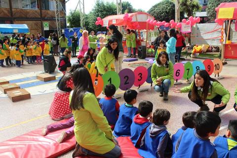 Un grupo de niños participan en actividades lúdicas al aire libre con monitores en un ambiente colorido.