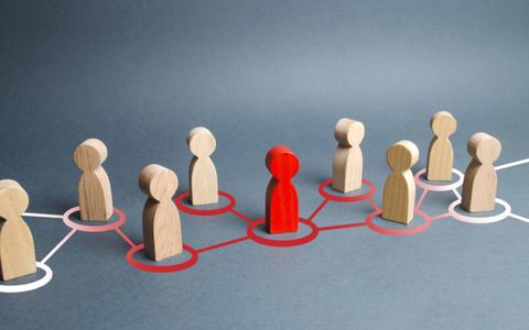 La imagen muestra figuras de madera que representan personas, donde una figura roja destaca en el centro de una red de figuras beige.