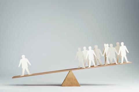 Una balanza de madera con figuras de papel que representan personas equilibrándose en lados opuestos.