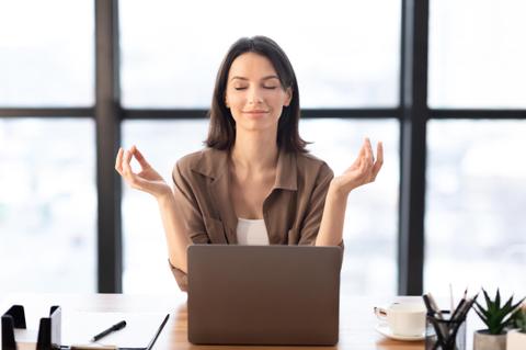 Mujer en posición de meditación frente a una computadora portátil.
