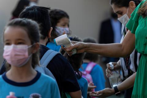Un grupo de niños en fila mientras un adulto les toma la temperatura con un termómetro.