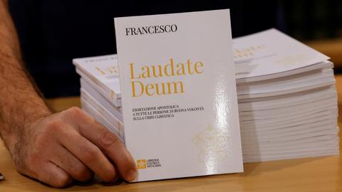 Un hombre sostiene un libro titulado 'Laudate Deum' junto a otros ejemplares apilados.