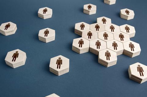 La imagen muestra fichas hexagonales de madera con figuras de personas grabadas en diferentes disposiciones sobre un fondo azul.