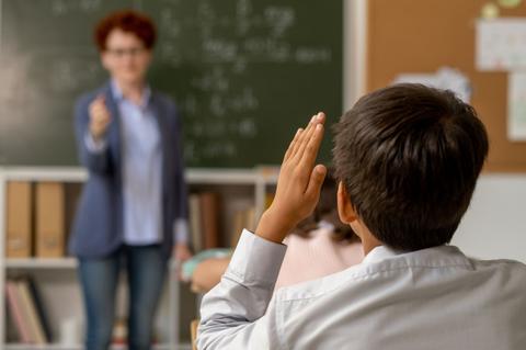 Un niño levanta la mano en clase mientras la maestra le observa.