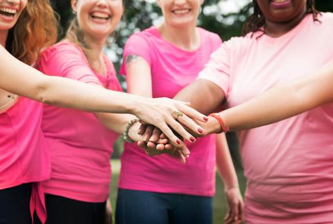 Un grupo de mujeres sonrientes con camisetas rosas se unen para dar un saludo de amistad.