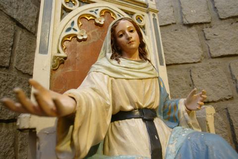 Escultura de una figura religiosa femenina sentada con los brazos extendidos.