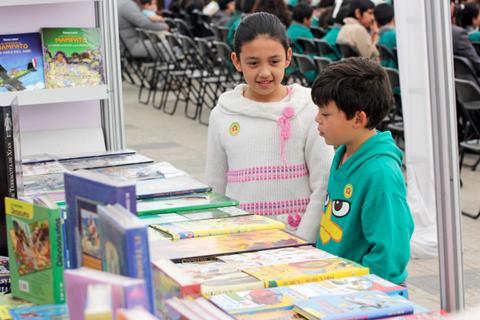 Dos niños observan una mesa llena de libros en un evento.