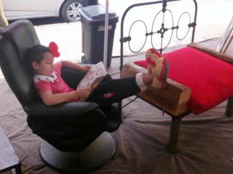 Un niño sentado en un sillón leyendo un libro con los pies en un mueble de madera.
