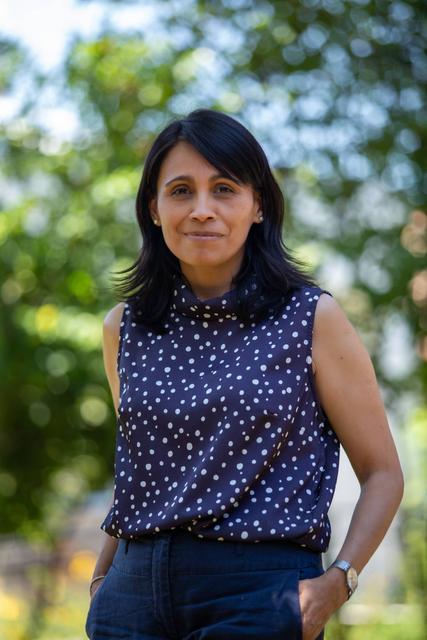 Una mujer sonriente con blusa de lunares en un entorno natural.