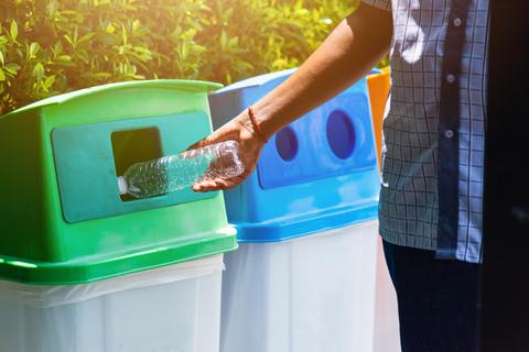 Una persona está desechando una botella de plástico en un contenedor de reciclaje.